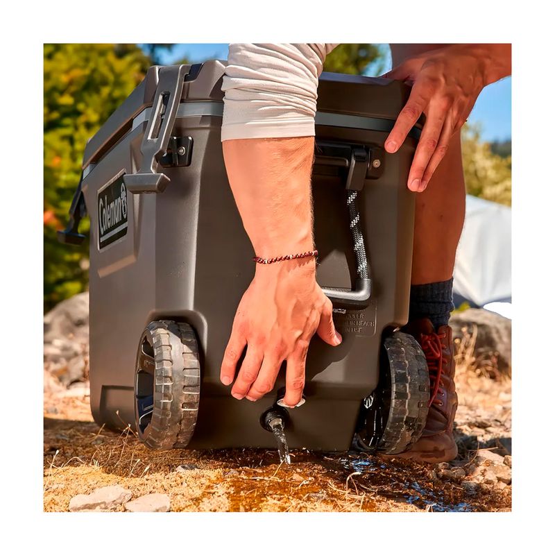 Hielera Convoy 65 qt con rueda negra Coleman, primer plano de la válvula de drenaje liberando agua en el suelo