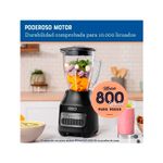 Licuadora vaso vidrio 1.5 l 800 W 6 vel gris Oster, equipo armado con frutas en el vaso y gráfico resaltando el motor