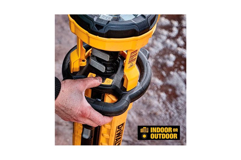Lámpara trípode 20V IP54 6Ah 3000 lúmenes DeWalt, detalle de mano accionando el botón de encendido en el cuerpo amarillo