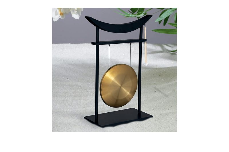 Figura decorativa Gong Toa 48 x 70 cm Atmosphera, vista frontal del gong dorado sobre soporte negro y fondo de arena