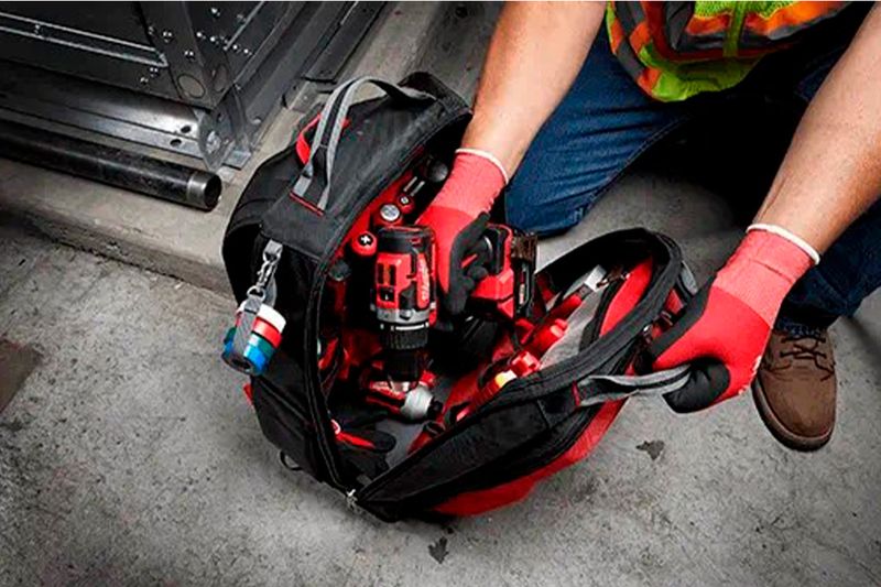 Mochila Packout 48 bolsillos Milwaukee, abierta mostrando un taladro rojo y herramientas en su interior