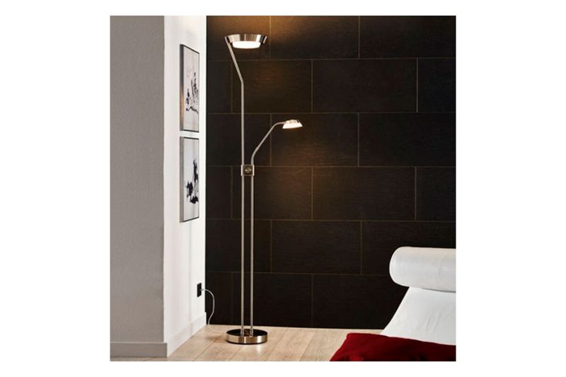 Lámpara de piso LED Sarrione cromo atenuable Eglo, encendida en ambiente interior junto a una pared negra y un sillón
