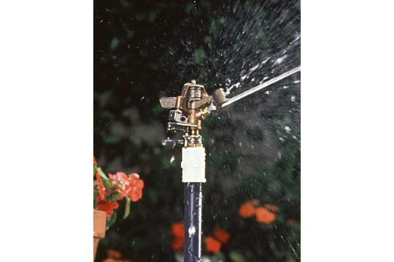 Aspersor para jardín de impacto Rain Bird bronce de 20-41 pies alcance, funcionando y lanzando agua en un jardín