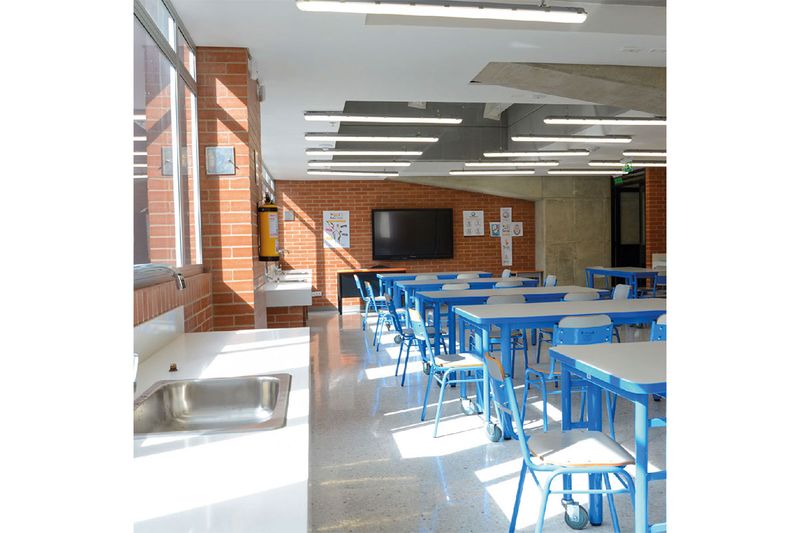 Luminaria LED hermética 36 W 6500 K 4500 lm IP65 IK05 Sylvania, instalada en el techo de un aula con mesas azules