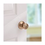 Cerradura pelota entrada Kwikset de latón antiguo, vista lateral instalada en puerta blanca con cerradura abierta